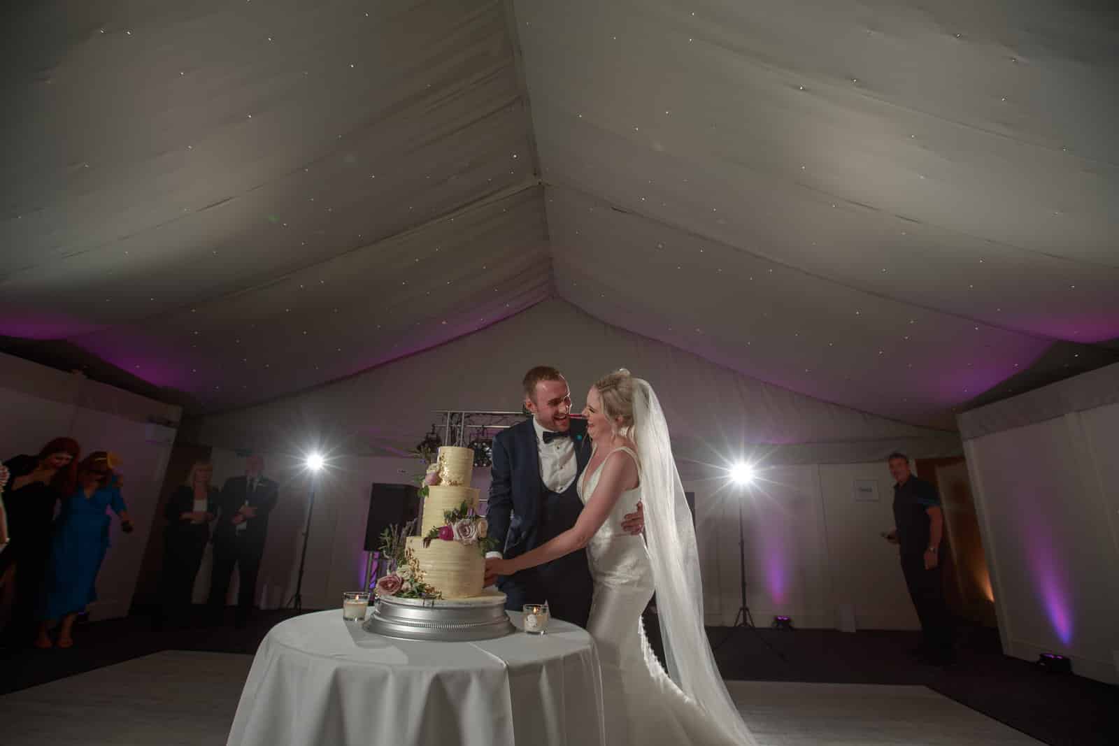 the happy newlyweds cut their wedding cake as the guests look on 