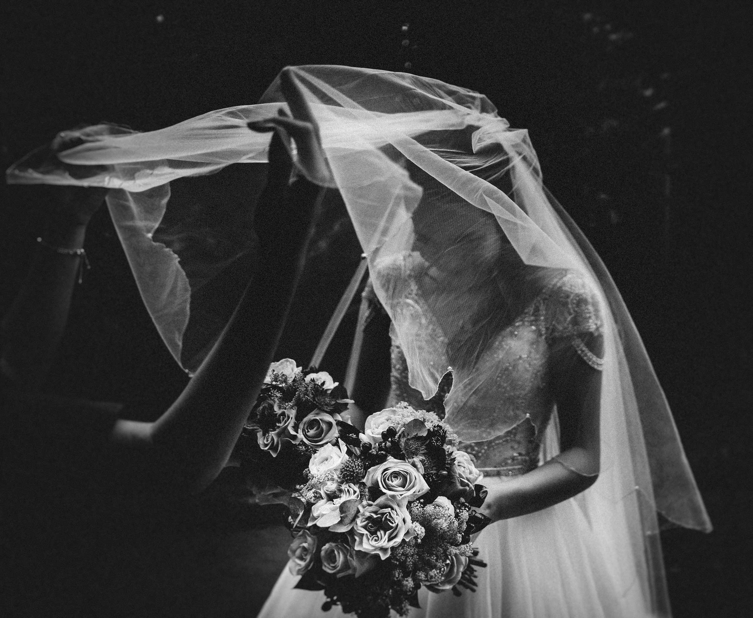 The beautiful bride has her veil placed over her by a bridesmaid.